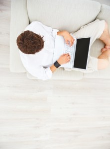 Top view of young guy sitting on sofa and working on laptop